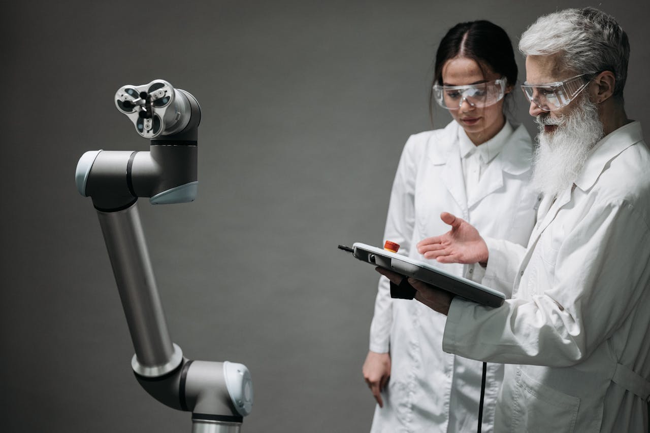 Researchers in lab coats and safety glasses engaging with a robotic arm in a lab setting.